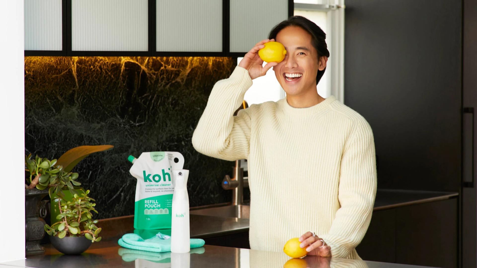 A man playfully holding a lemon in front of his eye in a kitchen, symbolizing the fun and eco-friendly approach of Koh's cleaning products