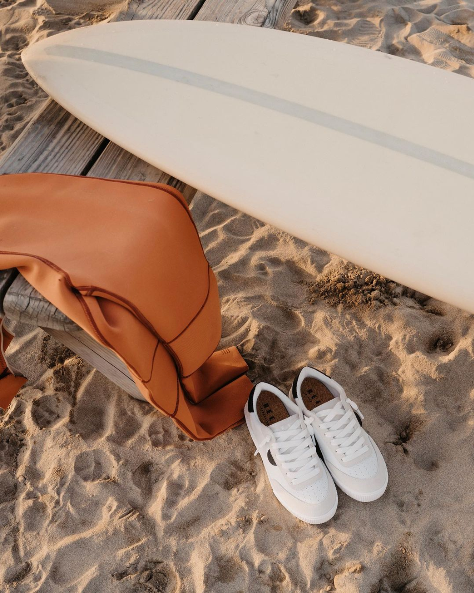 A pair of Reef brand shoes sitting on the sand next to a surfboard