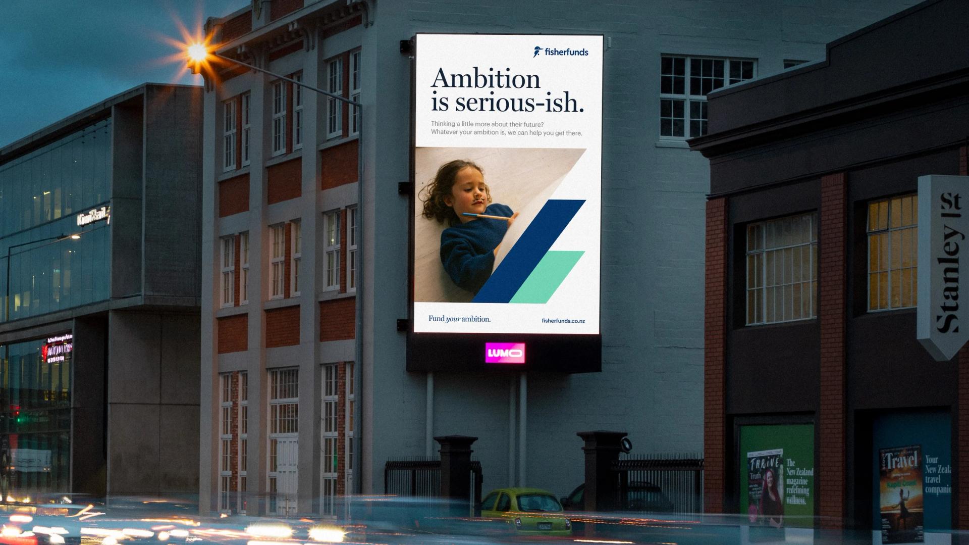 A billboard on the side of a building displaying Fisher Funds' brand campaign message 'Ambition is serious-ish', symbolizing their commitment to helping New Zealanders achieve their financial ambitions.