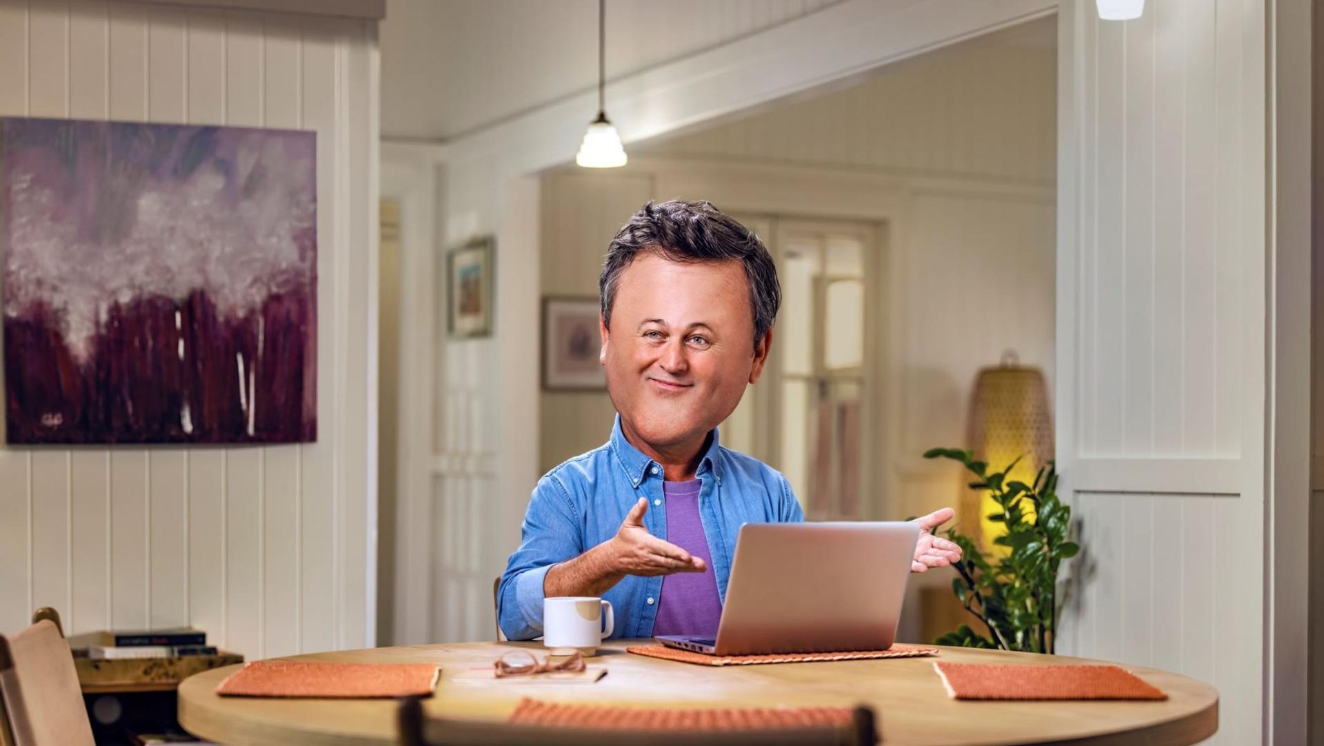 A man with a big head is sitting at a table with a laptop.