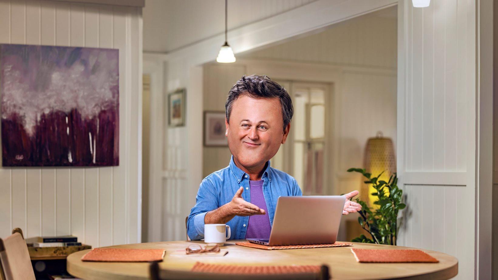 A man with a big head is sitting at a table with a laptop.