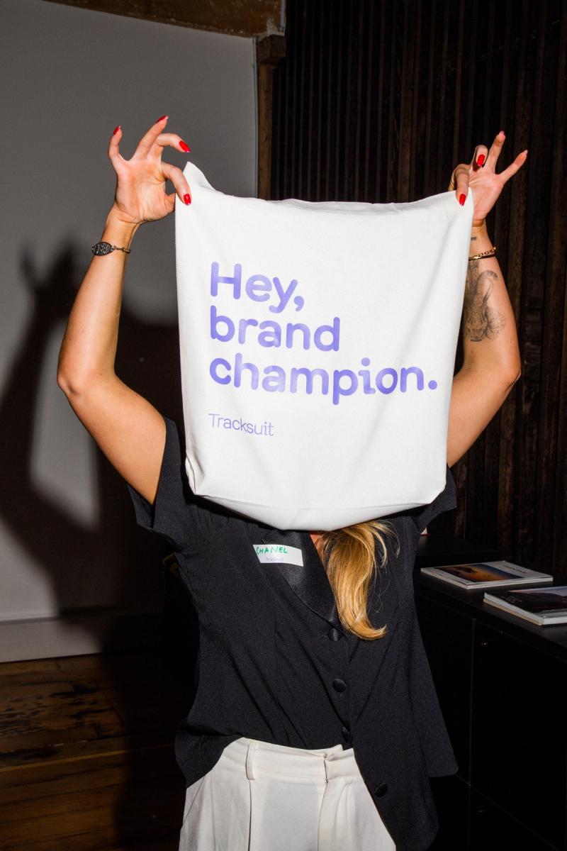 woman holding up a Tracksuit branded tote that reads "hey, brand champion"