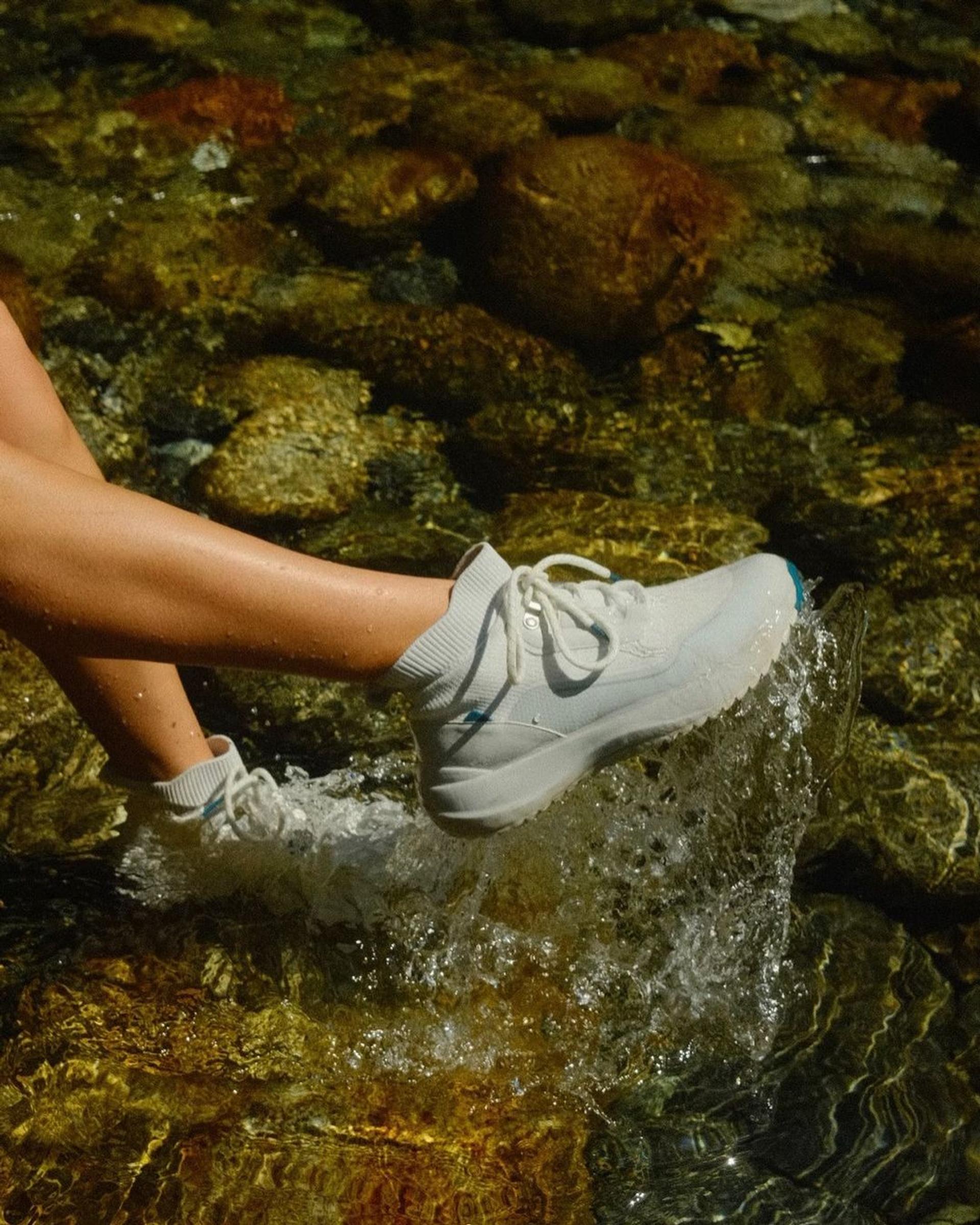 A person wearing Vessi's white waterproof shoes, the innovative footwear brand from Canada, walking through a river