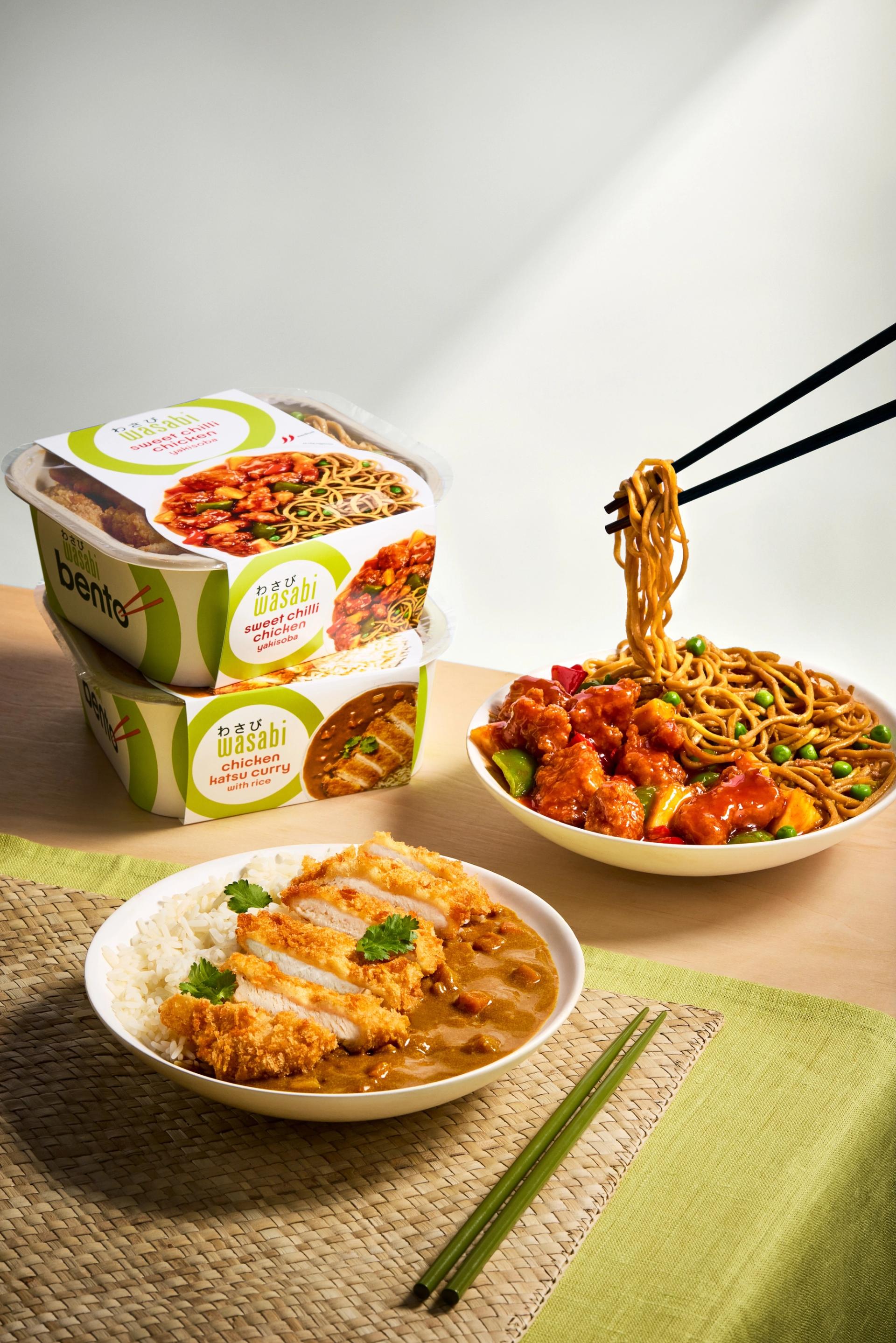 A stack of Wasabi's bento boxes neatly arranged on a table next to a plate of delicious Asian food, representing the brand's commitment to authentic flavors and convenient ready-made meals.