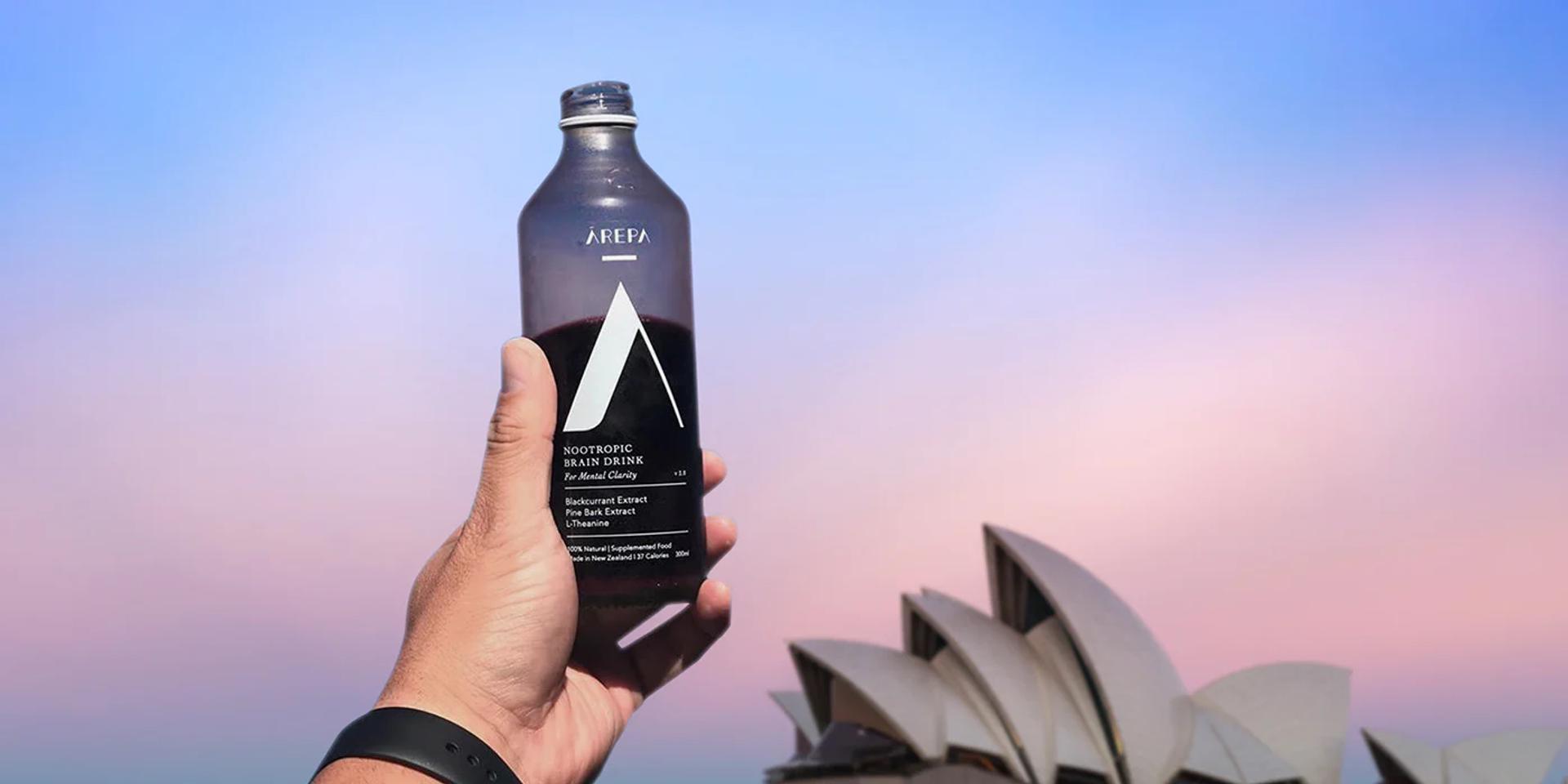 A person is holding a bottle of Arepa drink in front of the Opera House in Sydney