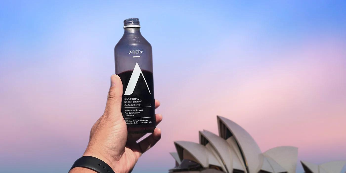 A person is holding a bottle of Arepa drink in front of the Opera House in Sydney