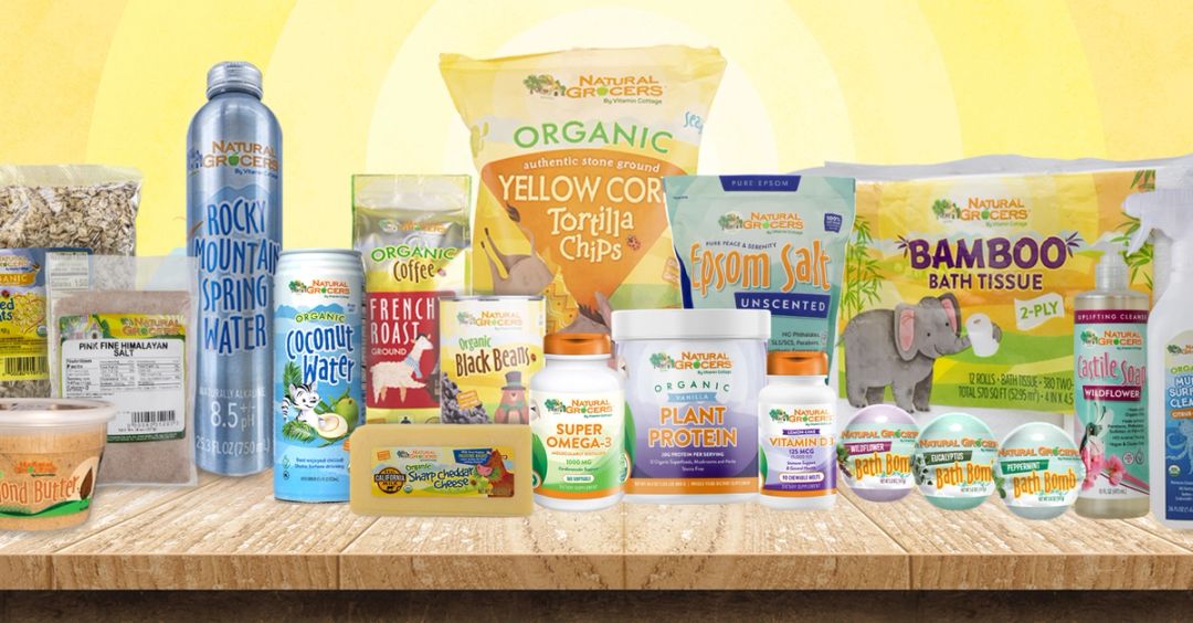 A shelf of Natural Grocers own-brand products, including tortilla chips, coconut water, coffee, supplements, bamboo bath tissue and bath bombs, against a sunny yellow background.