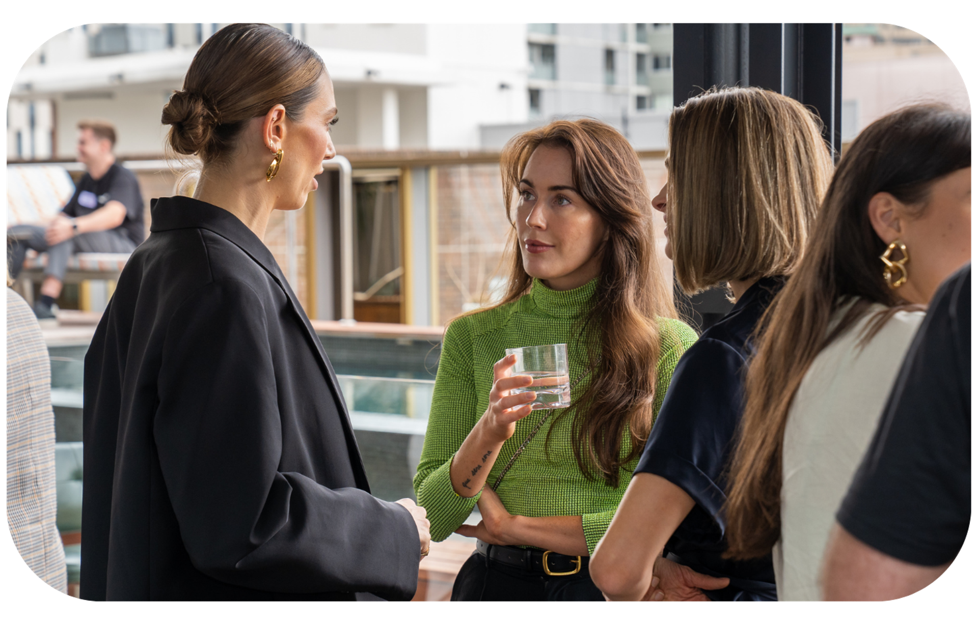 A professional woman in a green turtleneck holding a glass of water, symbolizing hydration and health in the workplace