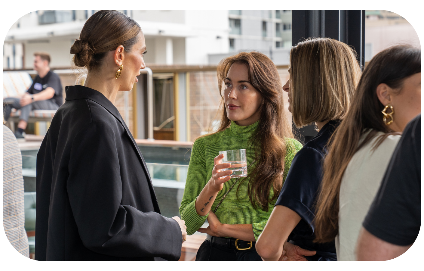 A professional woman in a green turtleneck holding a glass of water, symbolizing hydration and health in the workplace