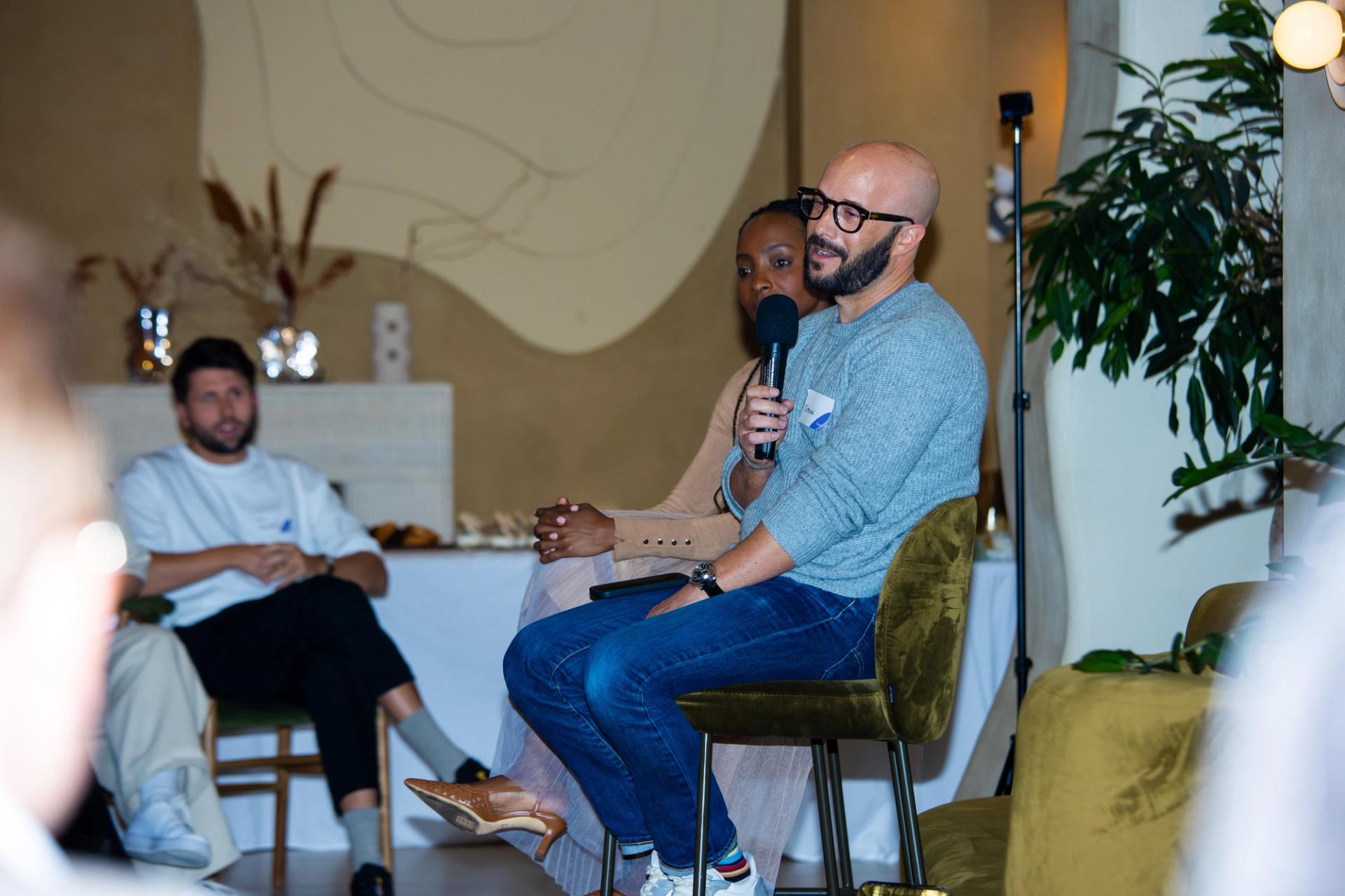 A man delivering a presentation on effective brand building strategies at the Building Brands of the Future event in London, holding a microphone while seated