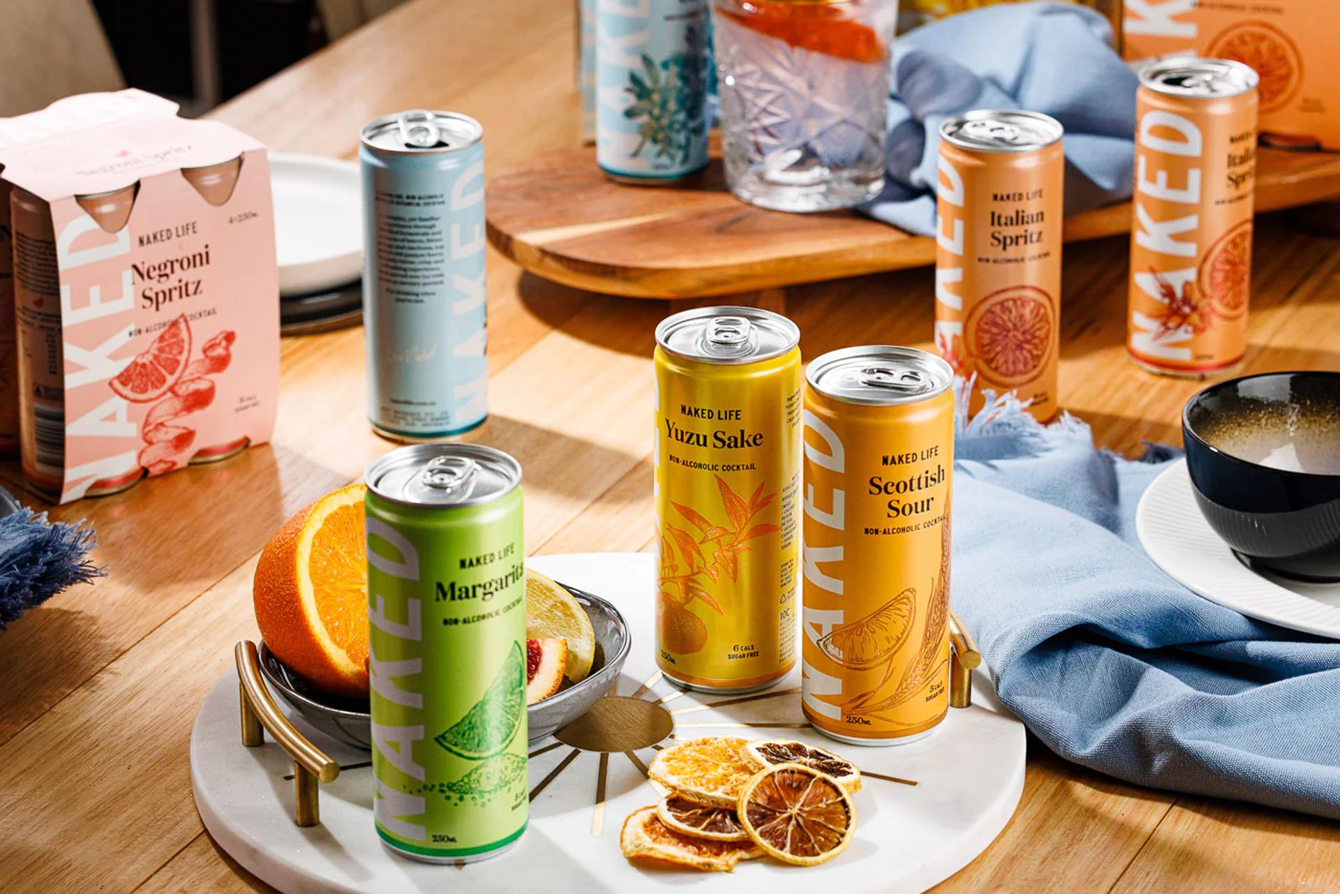 A table filled with a variety of canned drinks and fruit, featuring Naked Life product