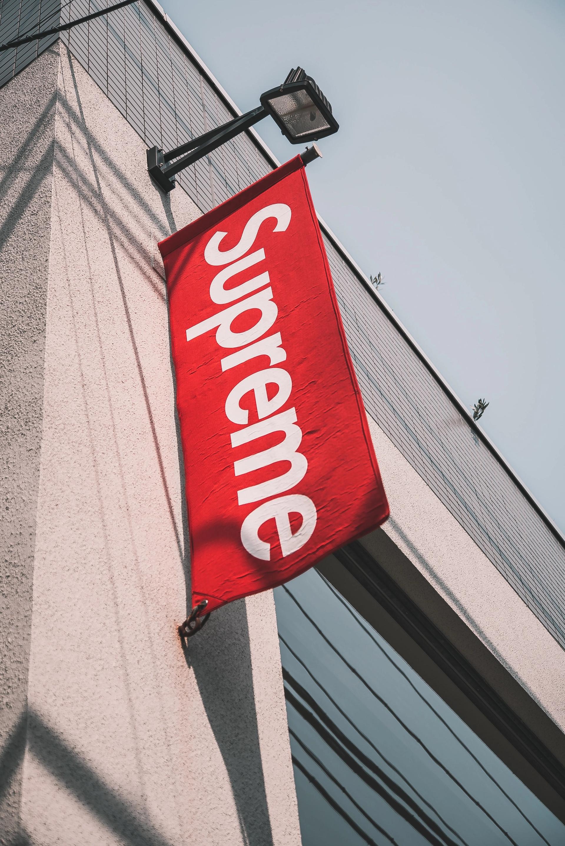 A red Supreme brand flag hanging from the side of a building, symbolizing brand presence and visibility in the urban environment.