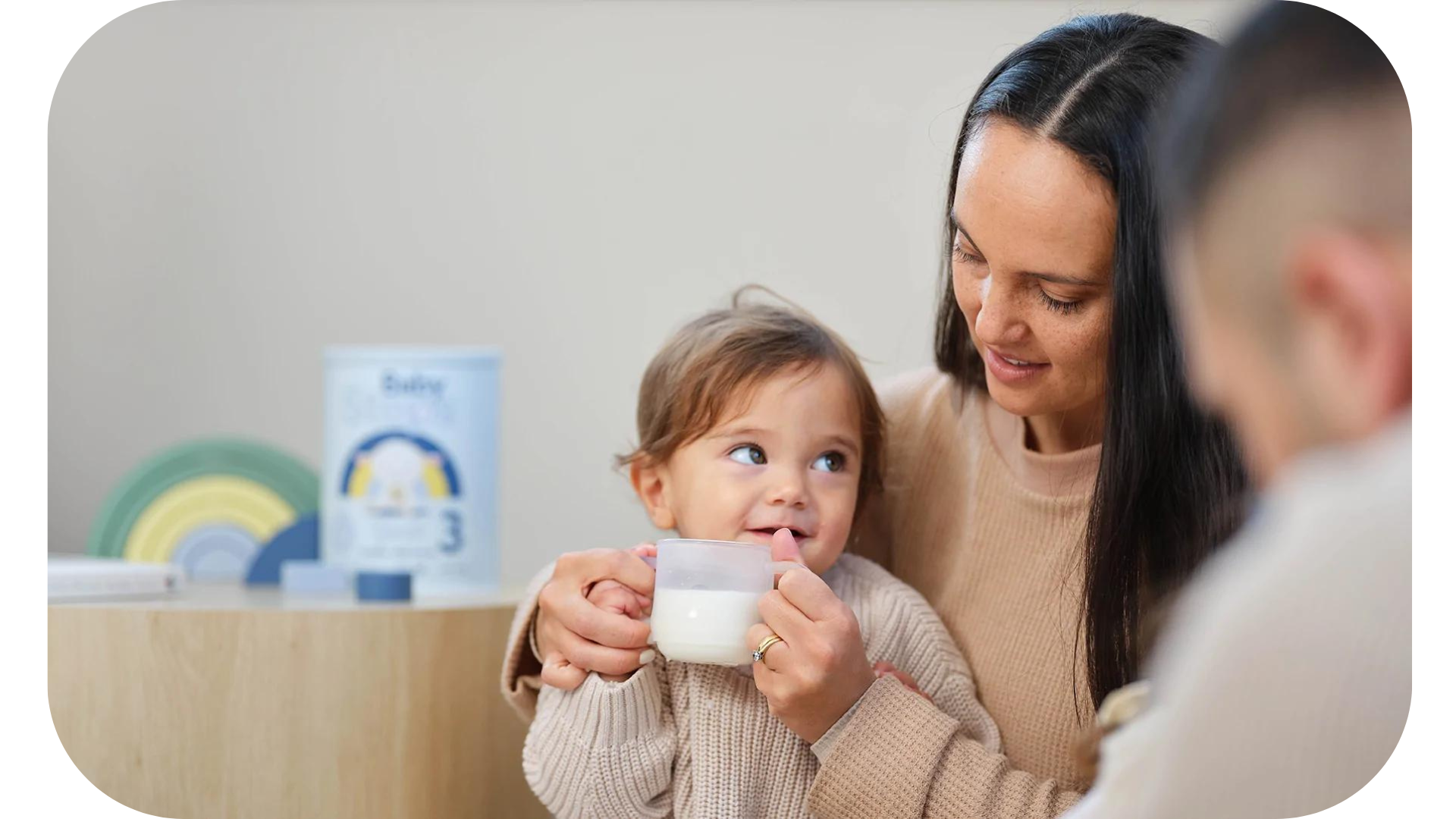 A mother lovingly holding her infant who is drinking goat's milk from a cup, symbolizing the Baby Steps brand's commitment to providing high-quality, nutritious alternatives for children.