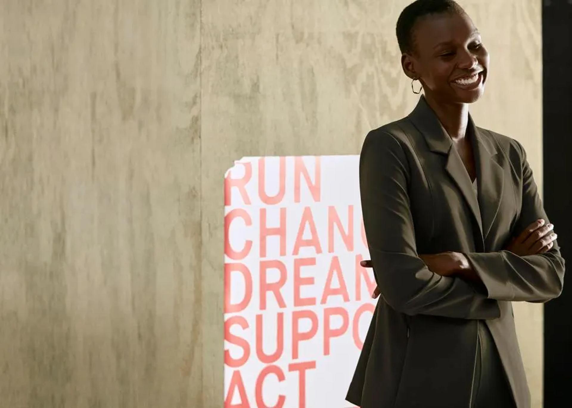 Maria Costa, Director of Brand and Integrated Marketing at M.M.LaFleur, standing confidently with crossed arms in front of a promotional poster