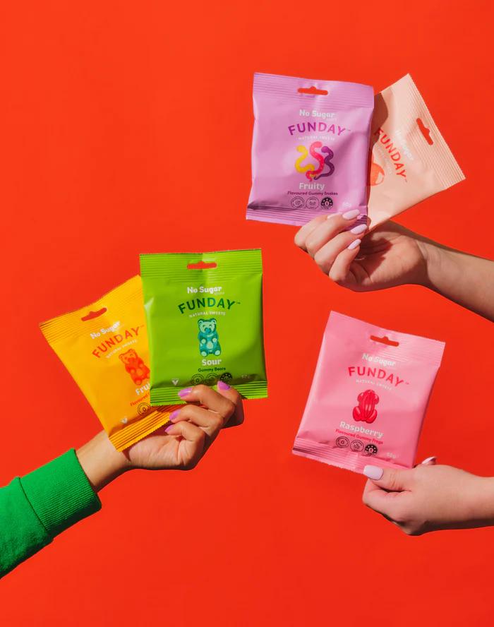 lineup of funday sweets packets with candy coming out of them on a pink background