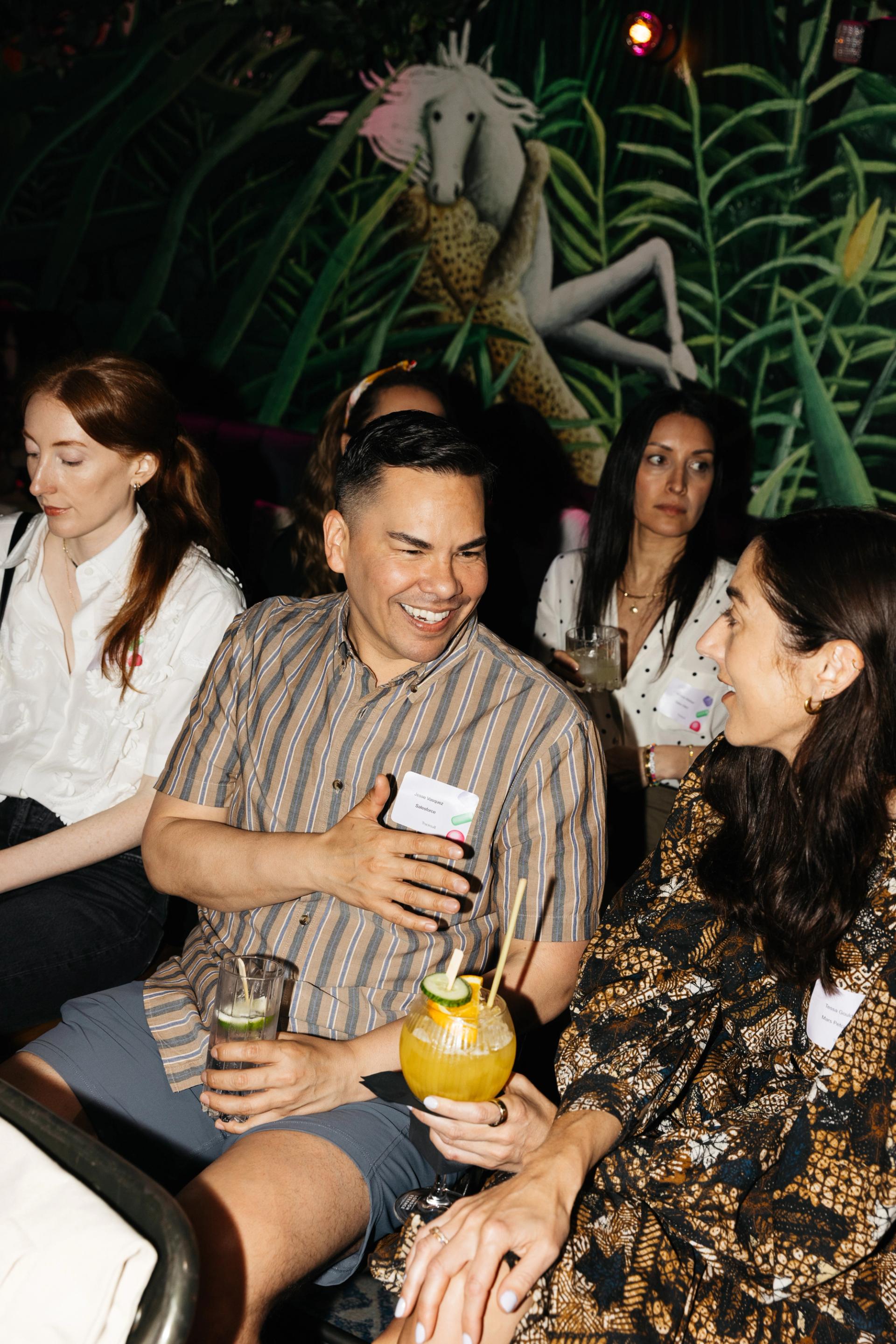 A diverse group of people engaged in a discussion during the 'Building Brands of the Future' event, sitting in front of a vibrant pink wall adorned with a unicorn mural, symbolizing creativity and uniqueness in brand building.