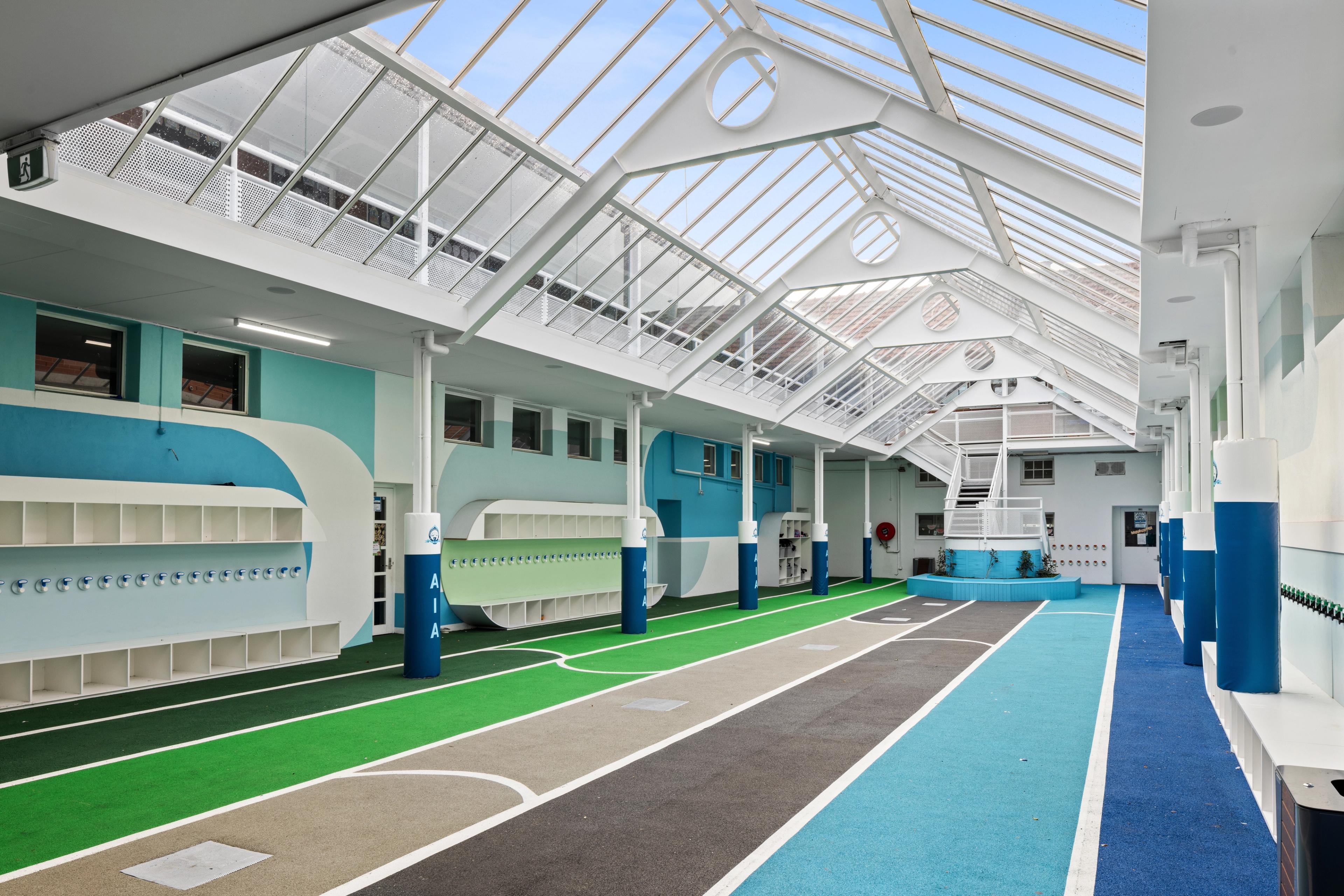 Bright indoor space with a glass roof, colorful striped floor, and blue and white walls with built-in cubbies.