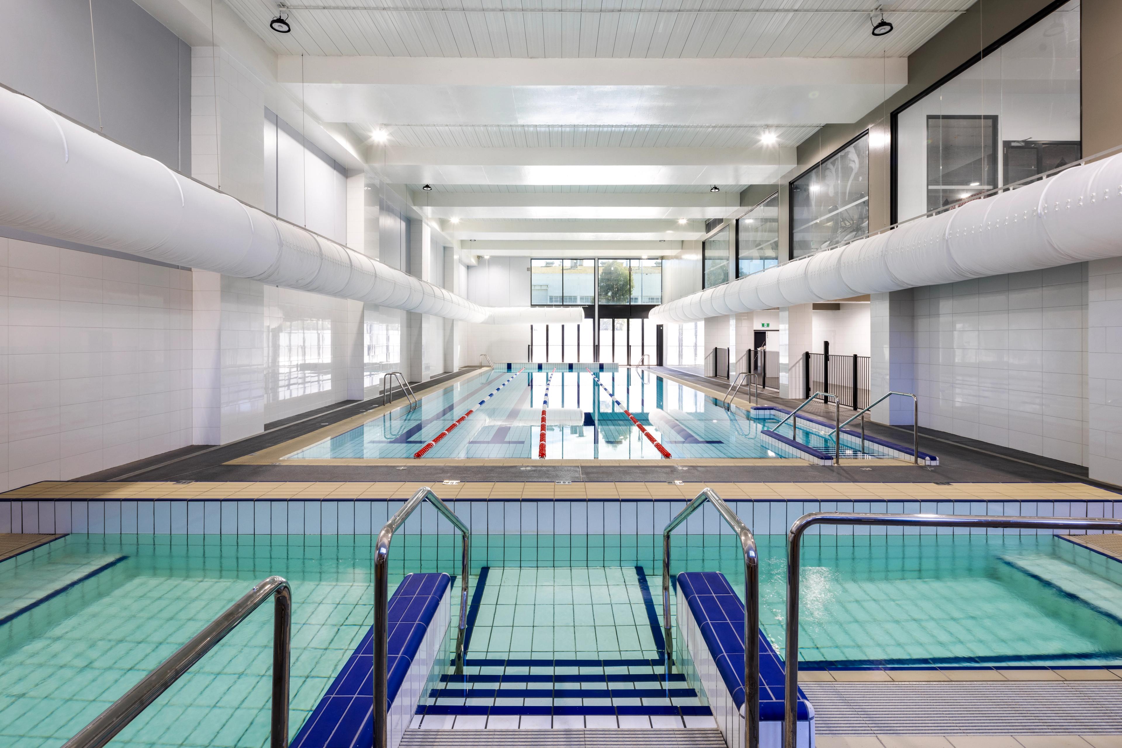 A bright, modern indoor swimming pool facility with a lap pool and two shallow entry pools.