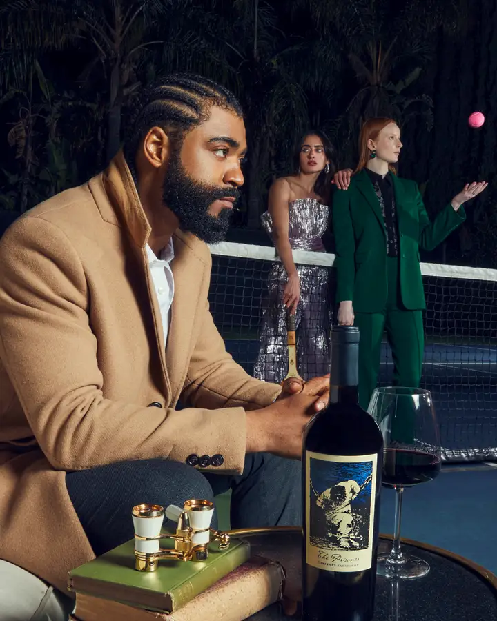 A group of diverse models gazes mysteriously into the distance. One of them sits near a stack of books and a pair of binoculars. The other two stand on either side of a tennis net, with one holding a racquet and the other throwing a ball into the air