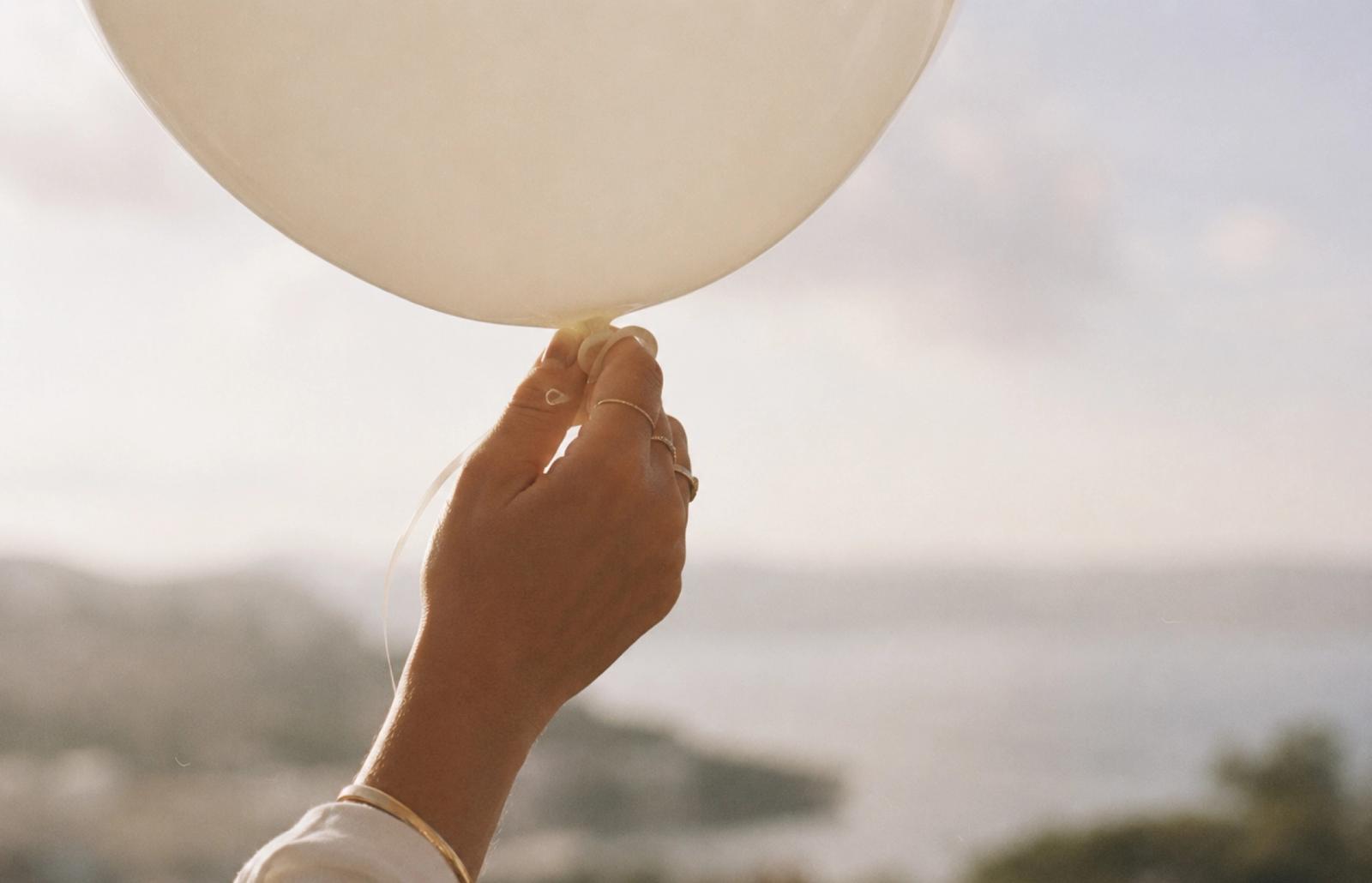 En hand håller en vit ballong med havet i bakgrunden.