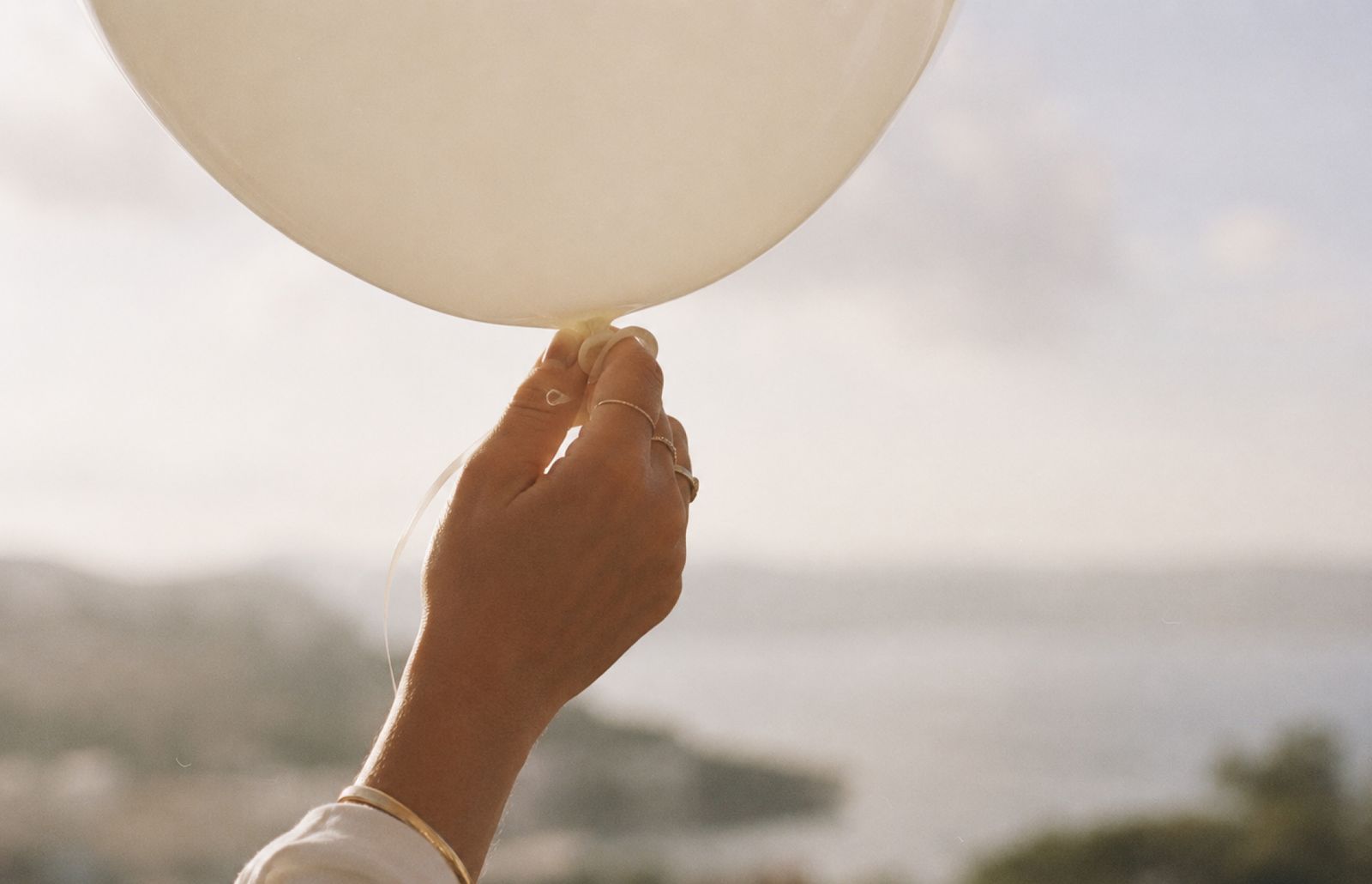 En hand håller en vit ballong med havet i bakgrunden.