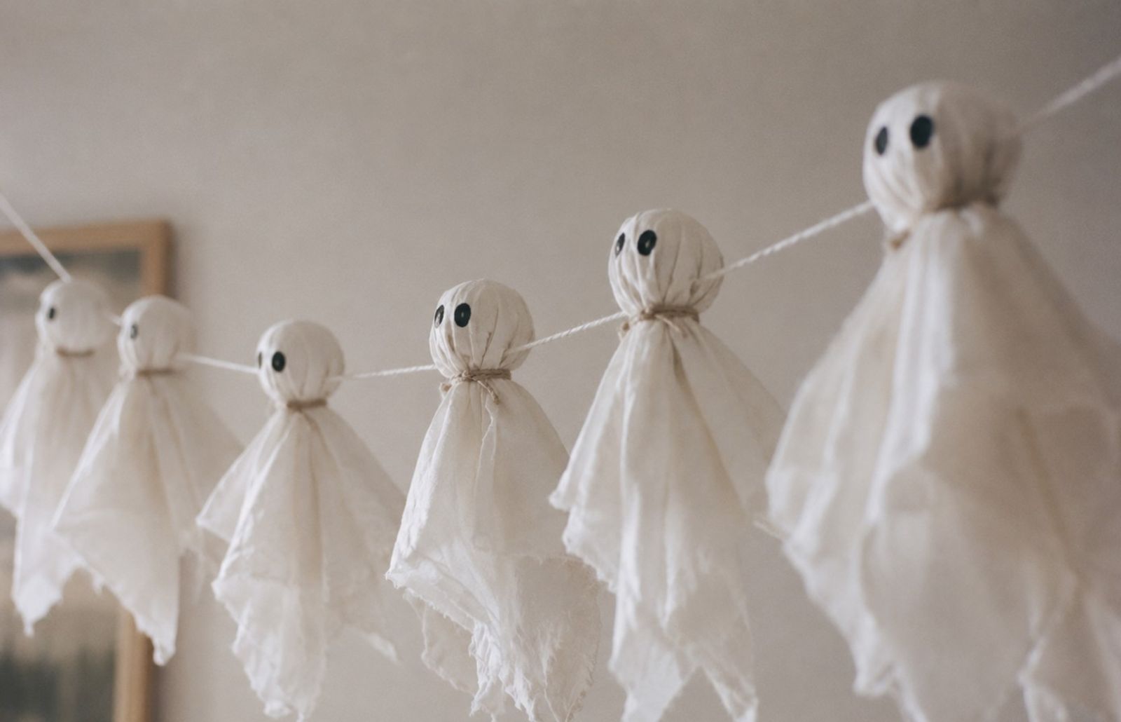 Hemmagjort halloweenpyssel, spöken av tyg som hänger i rad på ett snöre.