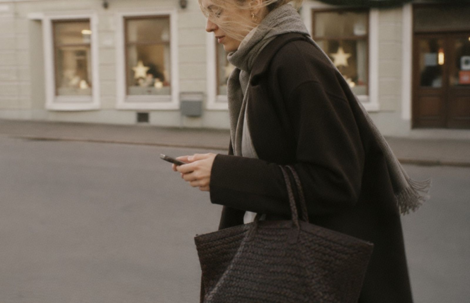 En jäktad kvinna klädd i svart med telefonen i handen på en gata.