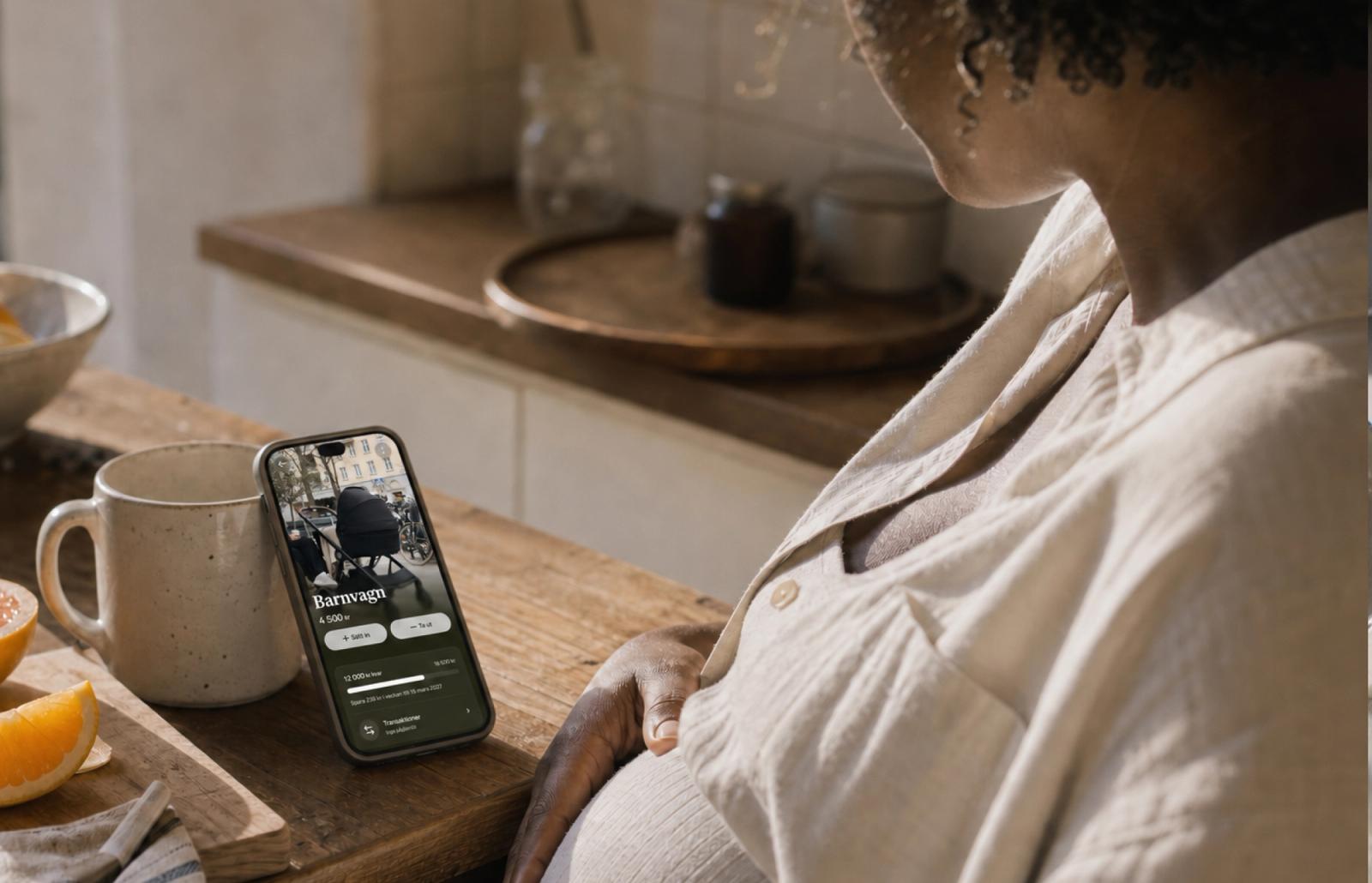 En gravid person tittar på en mobiltelefon som visar en Dreams-dröm för en barnvagn.