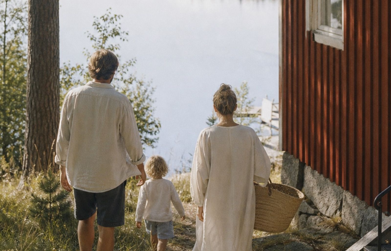 En familj med två föräldrar och ett barn som går bredvid en röd sommarstuga.