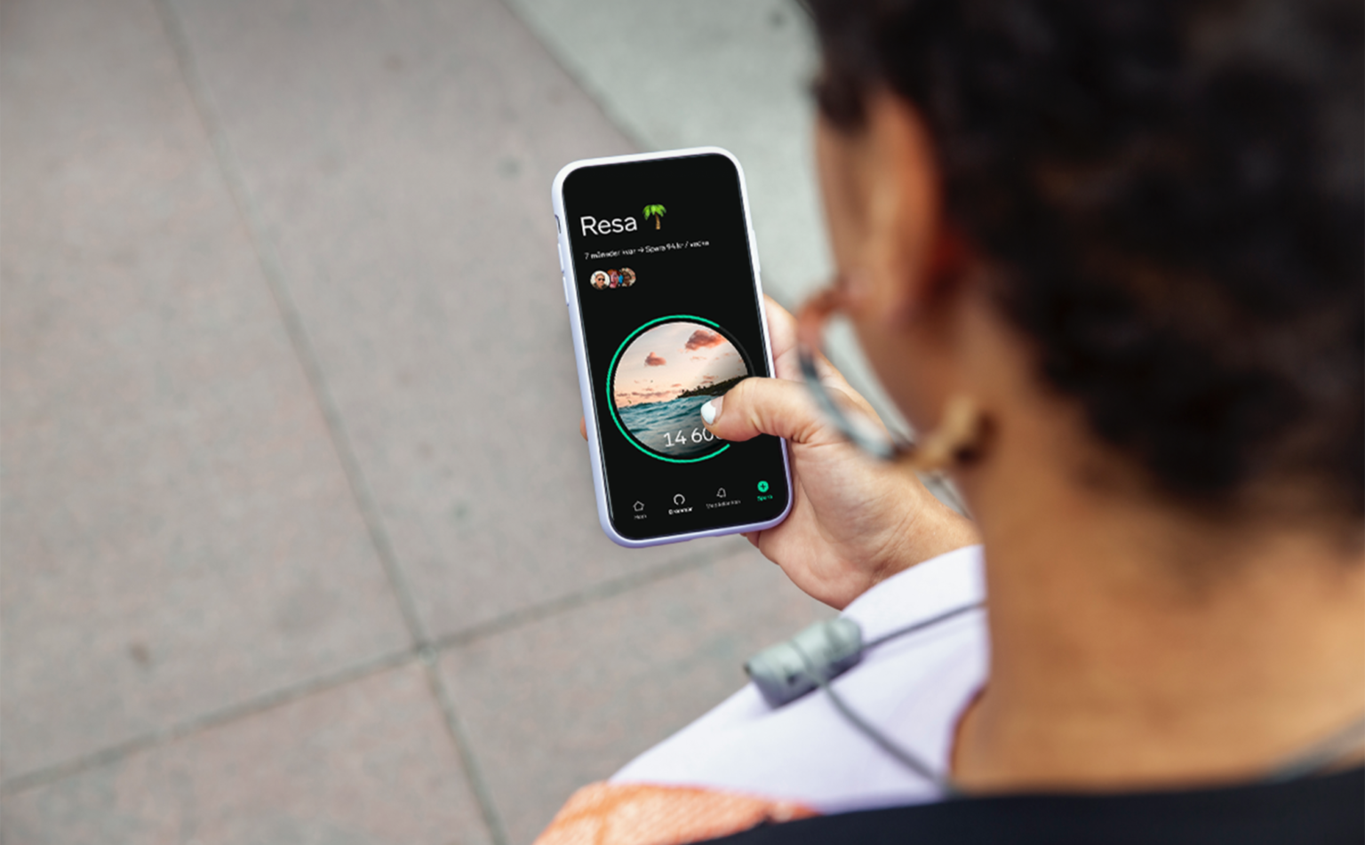 Person fotad bakifrån håller upp en mobiltelefon med Dreamsappens spardröm "Resa" öppen.