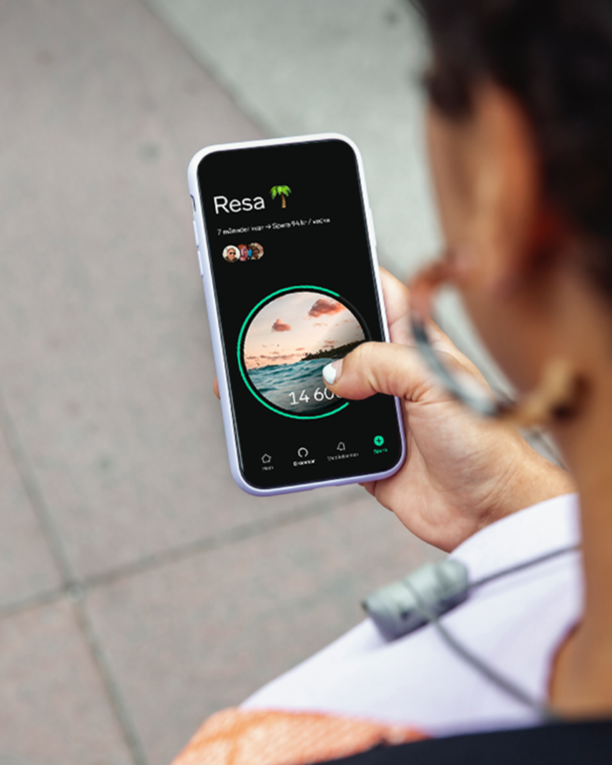 Person fotad bakifrån håller upp en mobiltelefon med Dreamsappens spardröm "Resa" öppen.