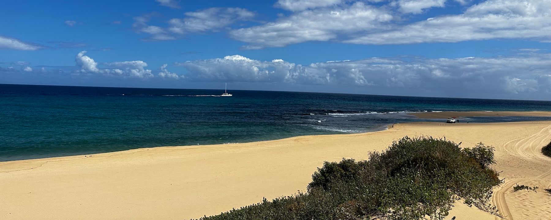 Vast expanse of golden sand stretching along Polihale State Park with deep blue ocean and distant sailboat