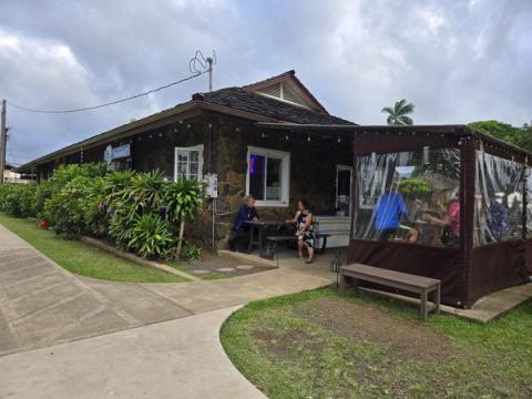 Charming stone-walled Kilauea Fish Market building with outdoor seating amid tropical landscaping