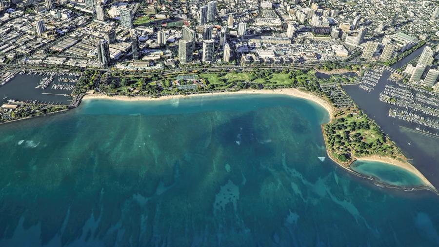 Aerial view of Ala Moana Beach Park in Honolulu, with a sandy shoreline, turquoise water, marinas, and nearby high-rise buildings.