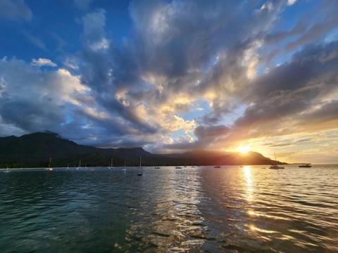Spectacular sunset over Hanalei Bay with sailboats anchored in calm waters and dramatic mountain silhouettes