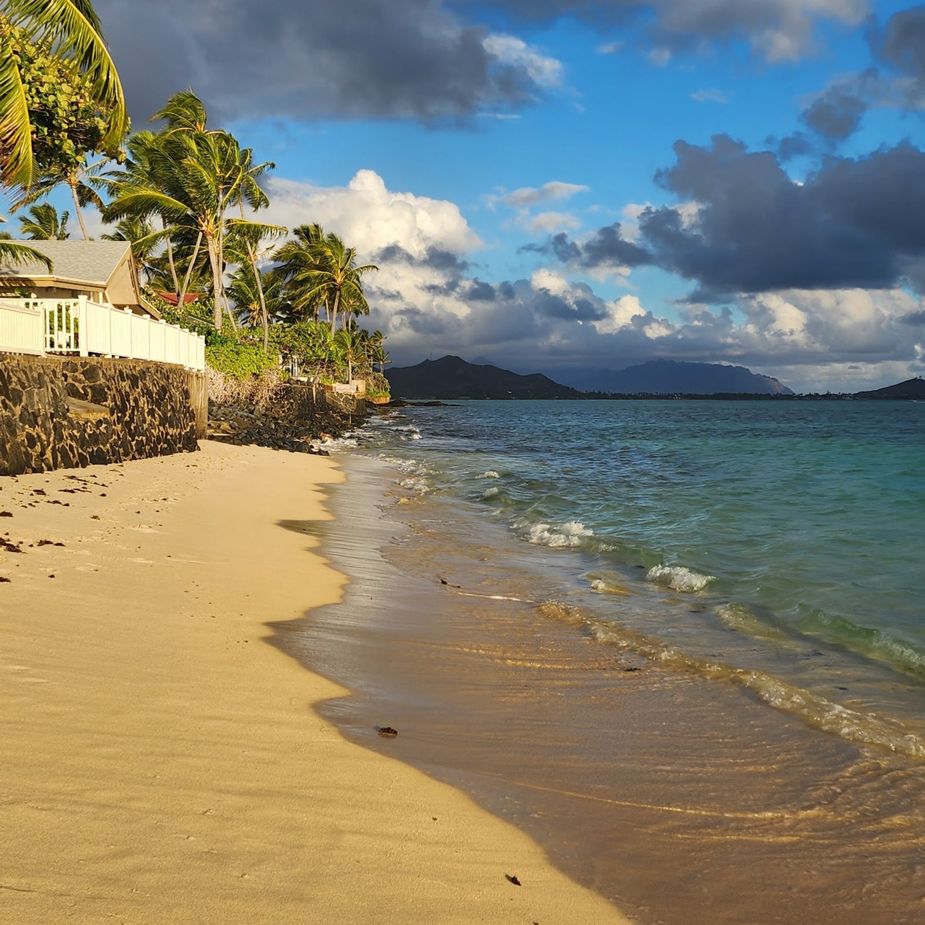 A quieter stretch of Lanikai Beach with residential shoreline, palms, and Windward Oahu views.