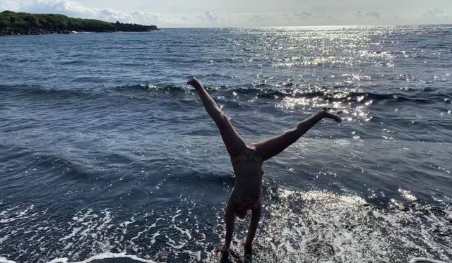 a young girl does a cartwheel on a black sand beach