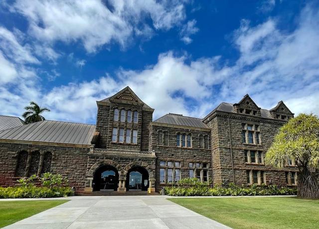 The historic Bishop Museum building framed by palms and greenery.