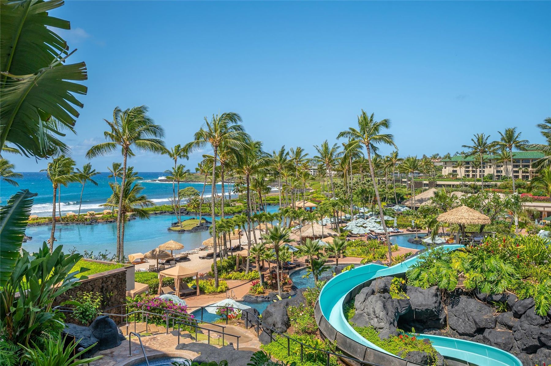 Aerial view of Grand Hyatt Kauai resort featuring a saltwater lagoon, waterslides, pools, and palm trees along the Poipu coastline