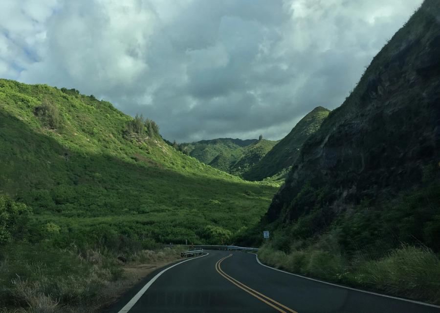 Winding two-lane road leading into a lush green mountain valley under heavy clouds in Maui.