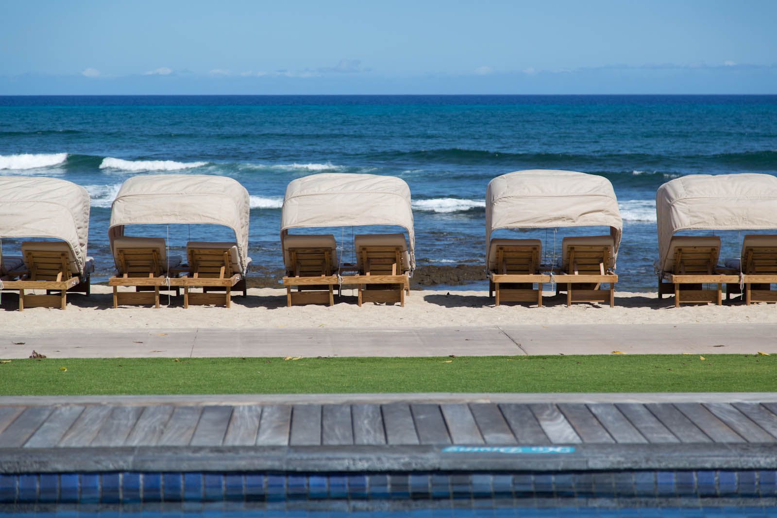 Covered lounge chairs lined up on a sandy beach facing the ocean in Kailua-Kona.