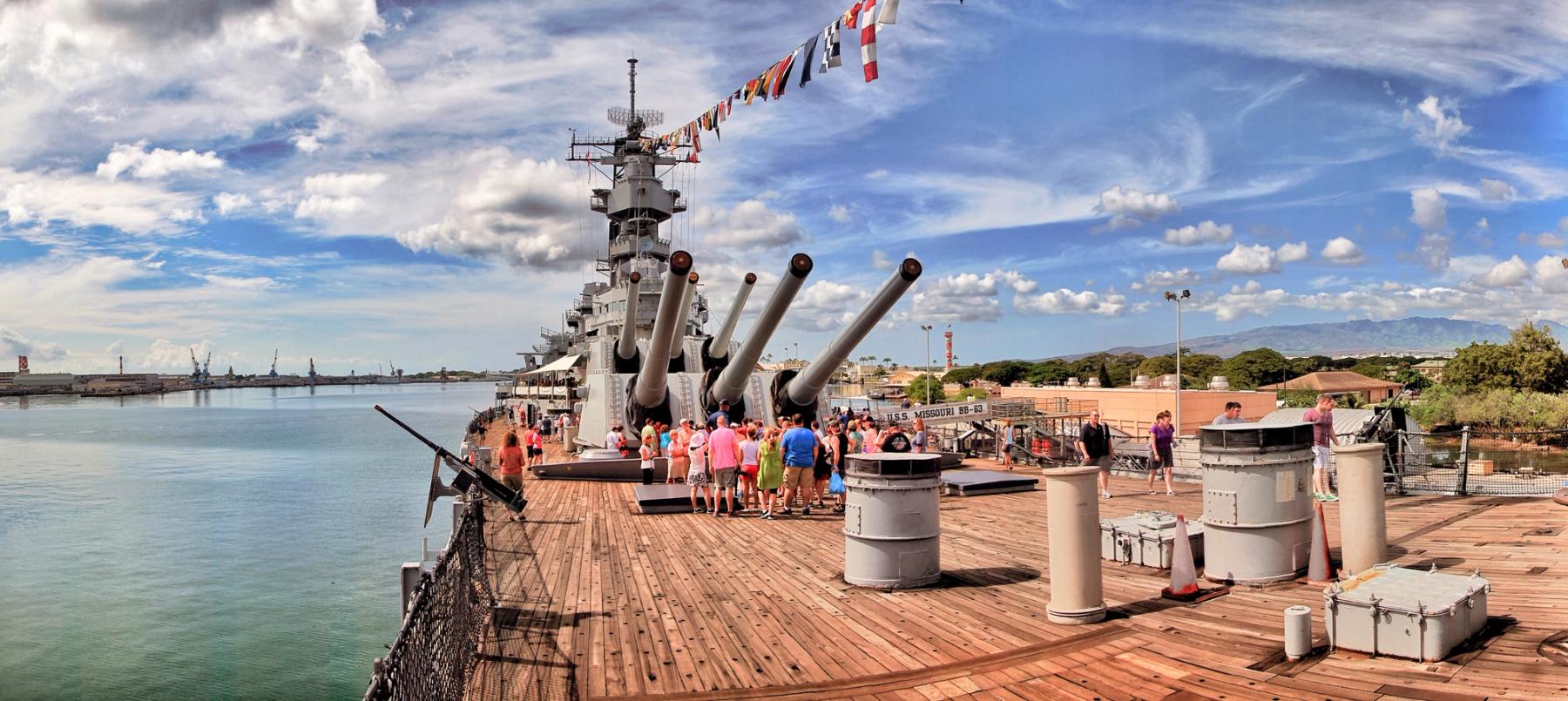 Visitors on the deck of the USS Missouri battleship near large gun turrets with signal flags overhead at Pearl Harbor on Oahu.