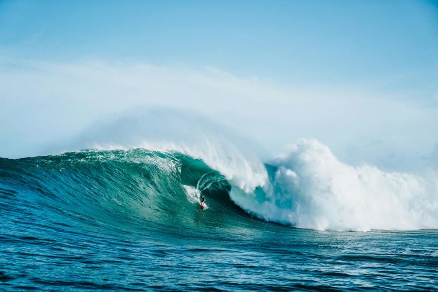 A surfer rides inside a large breaking ocean wave under a clear blue sky.