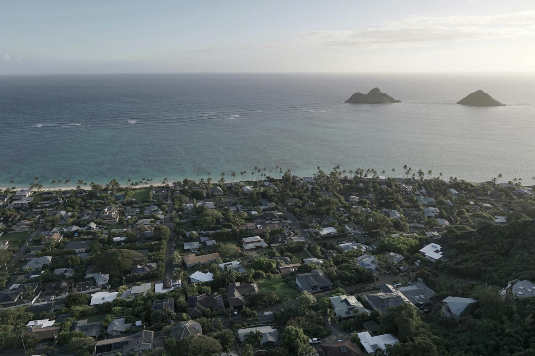 Aerial view of the Kailua and Lanikai shoreline on Oahu, with a neighborhood of homes and palm trees beside the ocean and offshore islets.