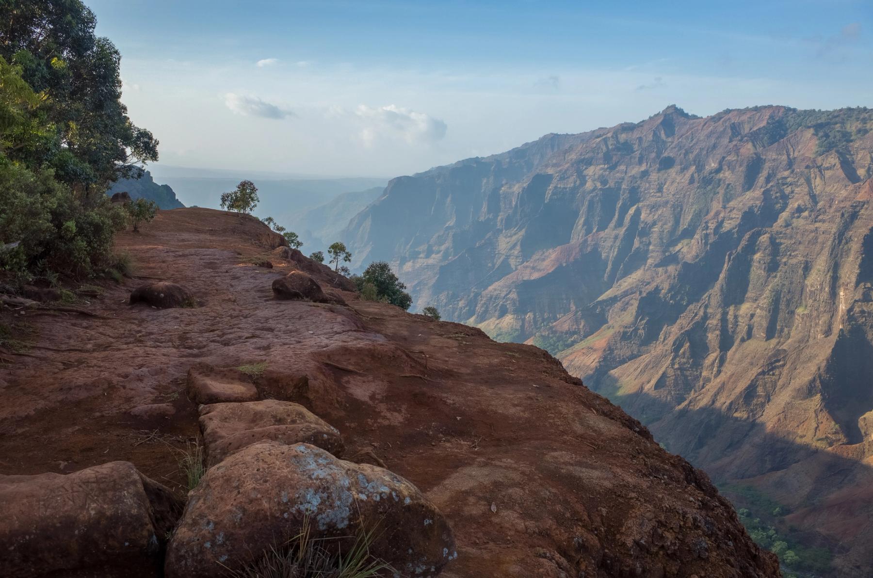 Rugged red rock ridge overlooking Waimea Canyon with layered cliffs and hazy morning sky
