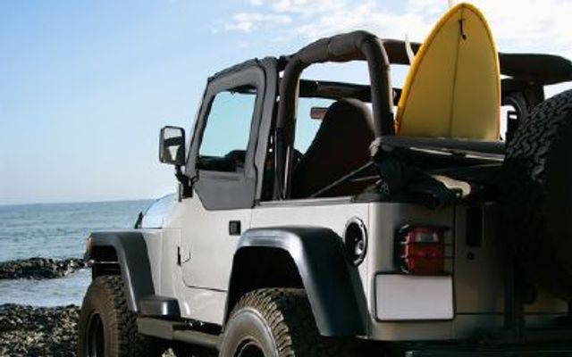 a Jeep parked at the beach with a surfboard in the back
