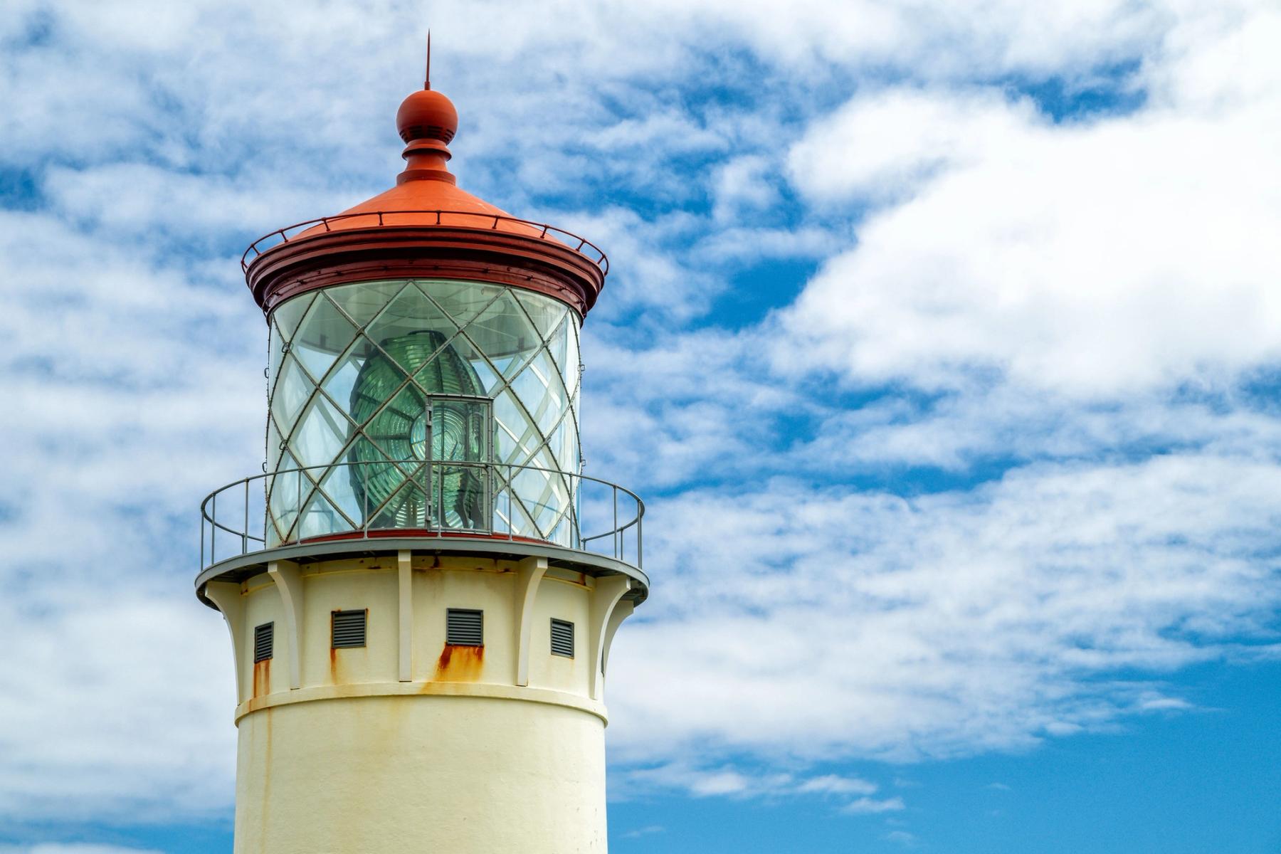 Close-up of the Kīlauea Lighthouse lantern room with red cap and glass lens against a blue sky with scattered clouds