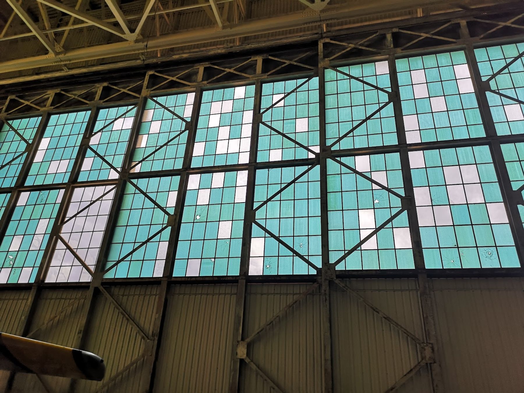 Bullet-marked blue glass windows inside a historic Pearl Harbor Aviation Museum hangar on Ford Island.