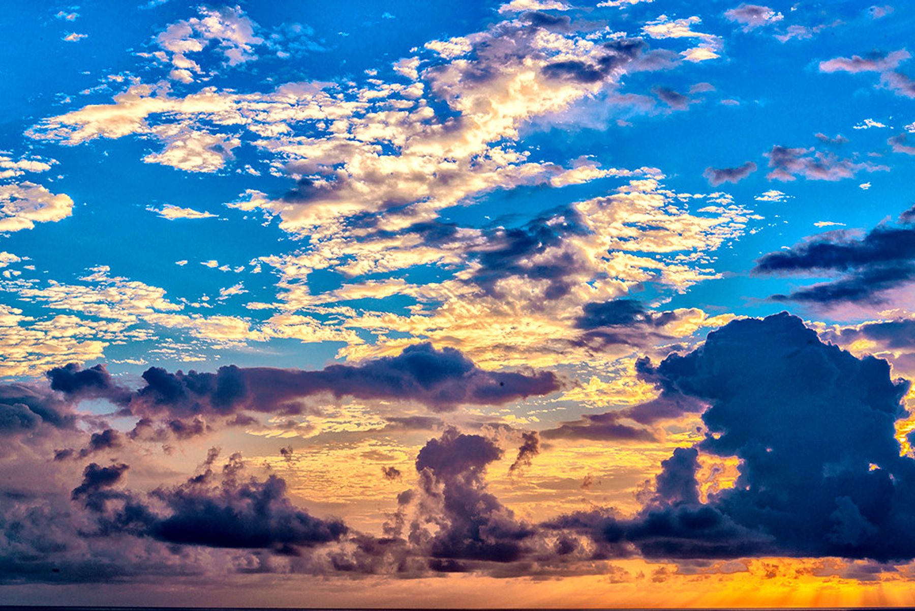 Golden sunset light illuminating layered clouds over the horizon, with deep blue sky and dark cloud silhouettes