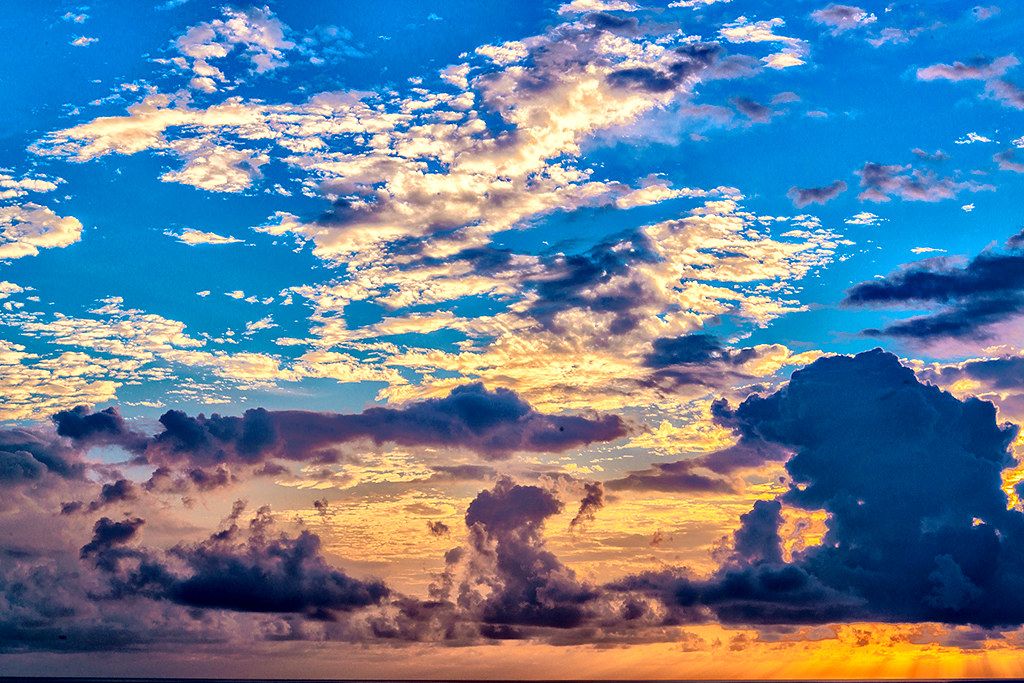 Golden sunset light illuminating layered clouds over the horizon, with deep blue sky and dark cloud silhouettes